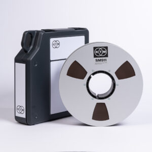 RTM SM911 R34420 2 tape on precision NAB reel stands upright by black RTM-logo case; both feature white branding.