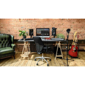 Modern music studio with computer, speakers, keyboard, guitars, Focusrite Clarett+ 4Pre interface on wood floor and brick wall.