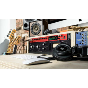 Modern music studio desk with headphones, keyboard, mouse, Clarett+ 8Pre interface, studio monitors, mics, and electric guitars by a brick wall.