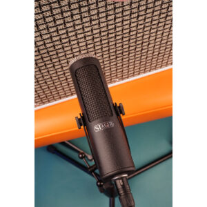 Stager SR-5 ribbon microphone on stand before a woven grille amp with orange trim, set against a teal backdrop.