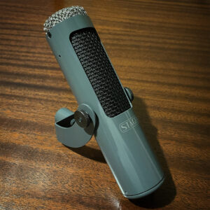 Stager SR-5 gray cylindrical ribbon microphone with mesh grille, logo on front, mounted on desk stand over wooden surface.