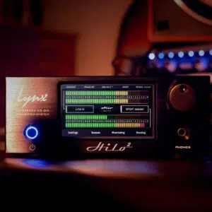 Lynx Hilo touchscreen audio interface glows on a studio desk, displaying input levels; pro-grade AD/DA, desktop silver unit.