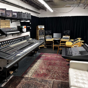 Professional studio with large consoles, keyboards, monitors, shelves, rugs, two wooden chairs, and a white sofa.