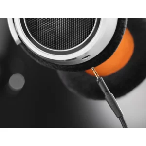 Close-up of a Neumann NDH 30 headphone earcup in sleek black and silver, featuring the signature orange interior and a detachable audio cable partially inserted into the jack—available now at Providence Sound And Vision.