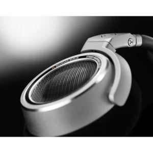 Close-up of the Neumann NDH 30 Open-Box silver and black open-back headphone earcup, featuring a precision-engineered mesh grill and prominent Neumann Berlin branding on the rim; showcased against a sleek black-and-white gradient background. Experience the exceptional design and renowned sound quality of Neumann headphones—available now at Providence Sound And Vision.