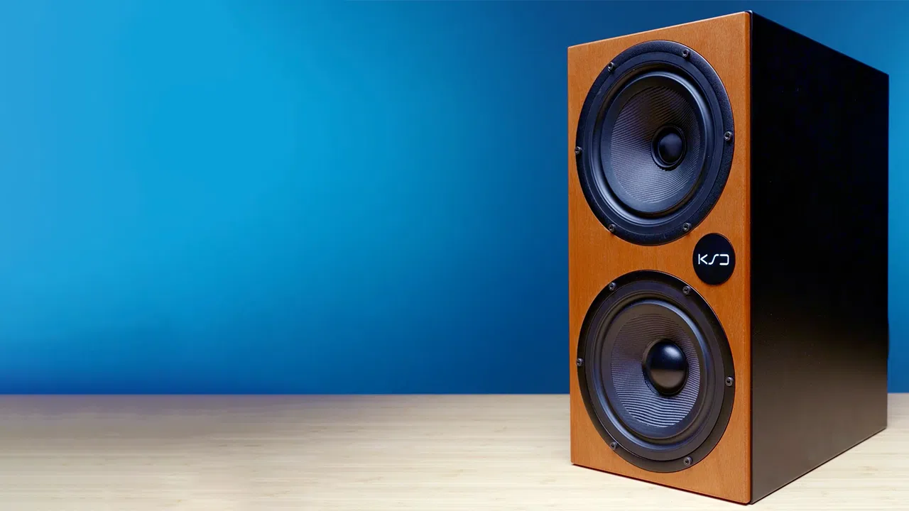 KSD C55 wooden speaker features dual black woofers and KJ logo, set on light wood with a blue gradient backdrop.