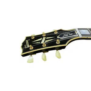 Black Gibson Custom 1957 Les Paul Reissue guitar headstock with gold tuners, white binding, and Les Paul Custom logo.