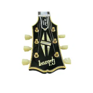 Black Gibson Custom 1957 Les Paul Reissue headstock, white tuners, gold hardware, mother-of-pearl inlay on white background.