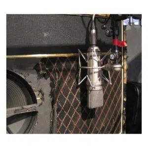 Neumann U 87 Ai Set Z condenser mic (open box) beside another mic in front of a worn guitar amp with red/gold diamond grille.