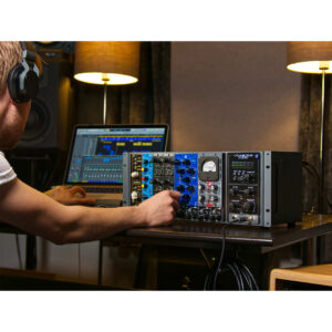 Engineer with headphones tunes Cranborne 500R8 rack unit by a laptop in a warmly lit studio with two modern lamps.