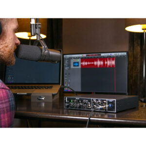 Person recording at desk with large mic, Cranborne Camden EC1 interface, laptop, and monitor showing audio waveforms.