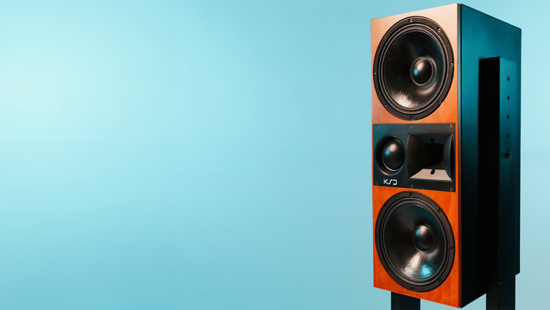KSD C55 wooden speaker with two black woofers, central coaxial driver, FIRTEC phase alignment, on light blue background.