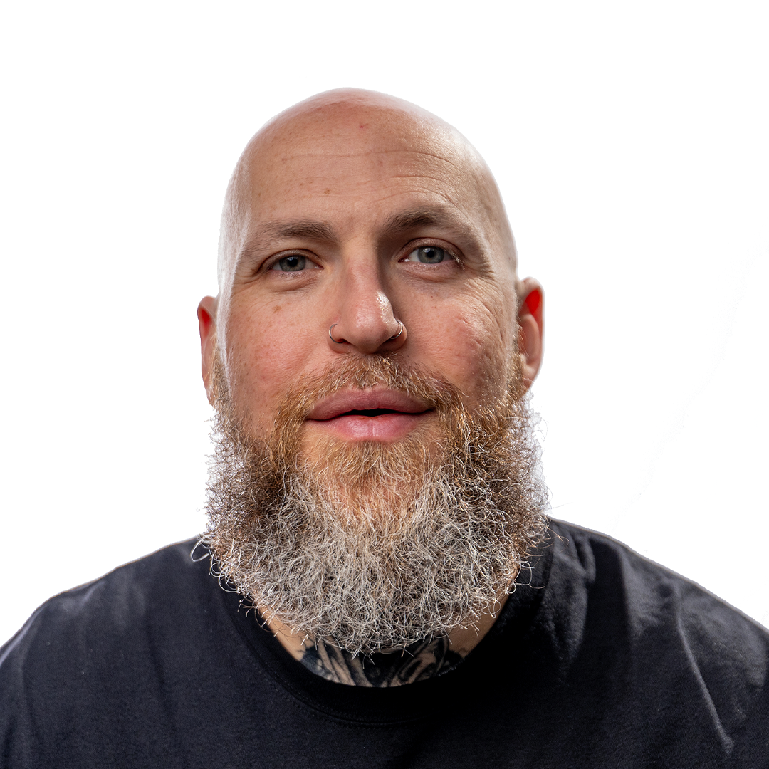 Bald man with a bushy gray beard and nose ring in a black shirt, facing camera against plain white background.