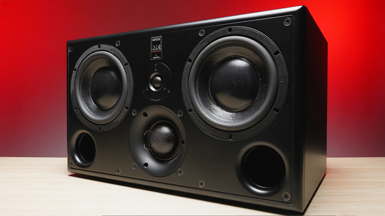 ATC SCM45A Pro black studio monitor with dual woofers and central tweeter on light wood, set against a bold red backdrop.