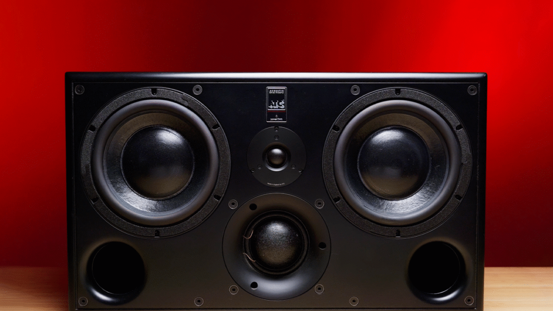 ATC SCM45A Pro black studio monitor with three drivers and dual ports rests on wood, set against a vivid red backdrop.