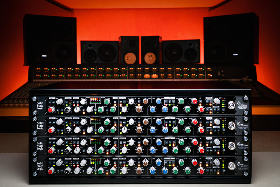 SSL Oracle rackmount units with colorful dials in a modern studio, large speakers and mixing console in the background.