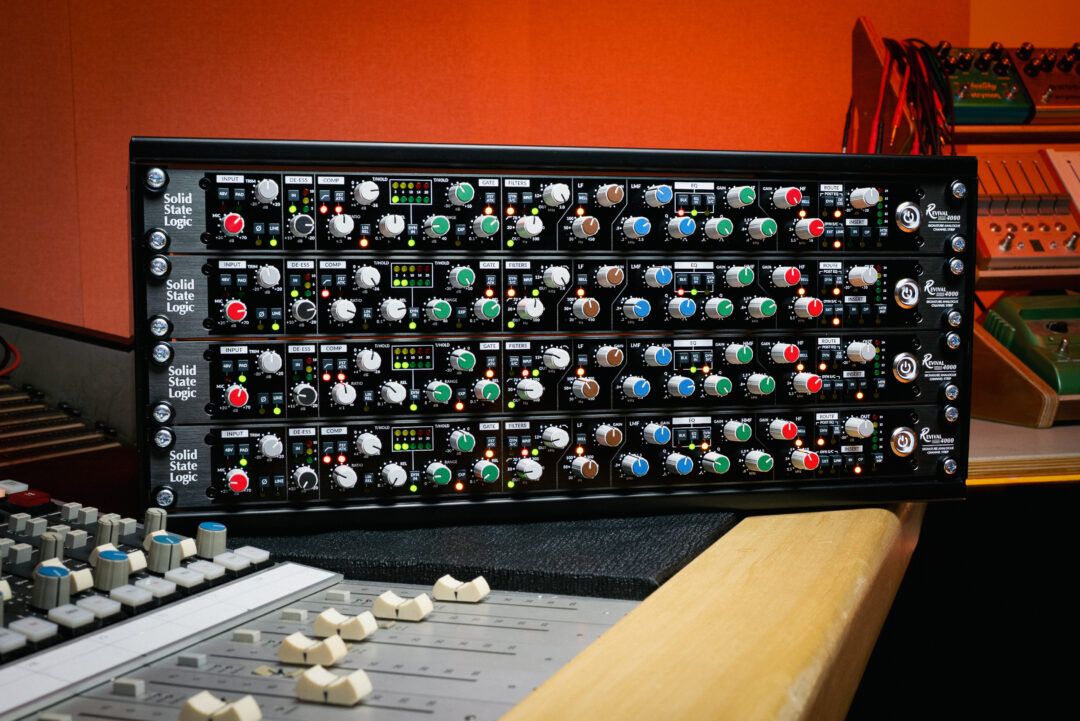 Solid State Logic SSL Oracle rackmount audio gear with colorful controls on a studio desk, surrounded by pro mixing faders.